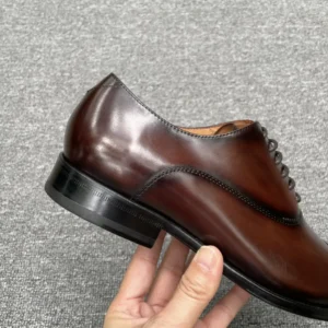 No brand visible brown leather dress shoe with black sole and classic design held by hand