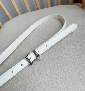Elegant white Prada Saffia belt with triangular metal logo decoration on a neutral fabric background.