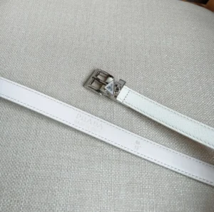 Elegant PRADA Saffia belt in white leather with triangular metal logo decoration on a textured background.