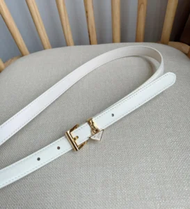 Elegant white PRADA belt featuring a triangular metal logo and gold buckle, displayed on a neutral fabric surface, emphasizing luxury and style.