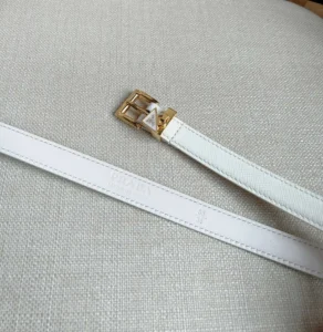 White PRADA belt with gold triangular logo buckle, elegant design, displayed on textured fabric background.