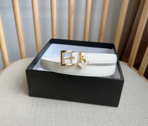 Elegant PRADA Saffia belt in a white finish, featuring a gold triangular logo buckle, presented in a black gift box, showcasing luxury design and craftsmanship.