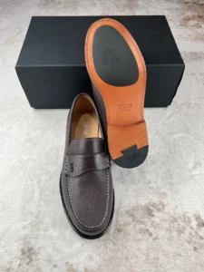 Dior Men's Boutique Le Fu Shoes, brown leather loafers with signature detailing, displayed atop a black shoe box, emphasizing luxury craftsmanship and urban style.