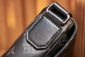 Close-up of the adjustable shoulder strap of a Louis Vuitton messenger bag, featuring Monogram Eclipse canvas and leather detailing, highlighting craftsmanship and luxury design.