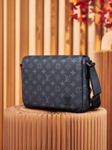 Louis Vuitton Dynamic Chip Version messenger bag in Monogram Eclipse canvas, featuring adjustable shoulder strap and visible LV logo, displayed on a textured pedestal.