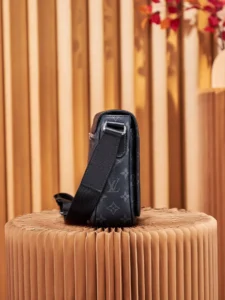 Louis Vuitton messenger bag in Monogram Eclipse canvas, showcasing adjustable shoulder strap and back zipper pocket, displayed on a textured pedestal.