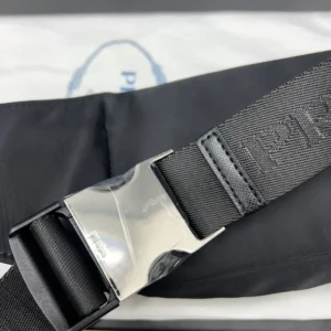 PRADA Re nylon waist bag strap detail featuring silver buckle and embossed logo on black fabric.
