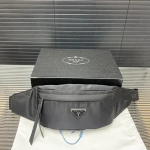 PRADA Re Nylon waist bag displayed on a white dust bag beside its black packaging, showcasing luxury craftsmanship and design.