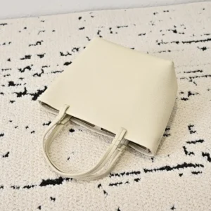 The Row Park tote in light beige leather on a textured surface, showcasing minimalist design and practical size for versatile use.