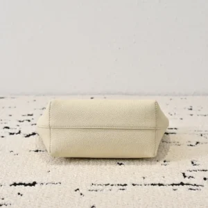 The Row Park tote bag in cream color, showcasing a minimalist design with lychee patterned cowhide texture, positioned on a textured surface.