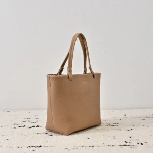 The Row Park tote bag in soft lychee patterned cowhide, showcasing minimalist design and neutral beige color, displayed on a textured surface.