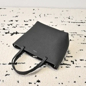 Black The Row Park tote bag on a textured surface, showcasing its sleek design and soft lychee patterned cowhide material, highlighting the bag's stylish and functional features.