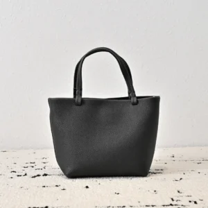 Black leather tote bag with two handles, featuring a structured design suitable for everyday use, highlighted as The Row Park Tote available for purchase.