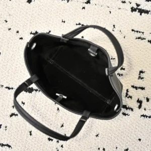 Interior view of The Row Park tote bag, showcasing black fabric lining and dual handles, placed on a textured surface.
