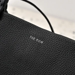 Close-up of The Row logo on textured black leather, showcasing the premium quality of The Row Park Tote, featured in an online fashion store.