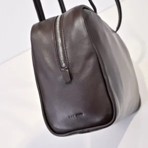 Shoulder bag featuring sleek design in dark brown sheepskin, showcasing zipper detail and brand logo for The Row Astra Bowling.