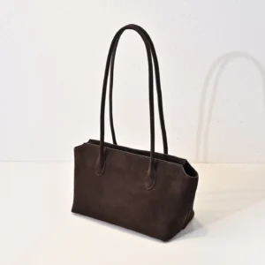 The Row Saddle leather shoulder bag in dark brown with long handles, showcasing soft, glossy calf leather texture, ideal for commuting and convenience.