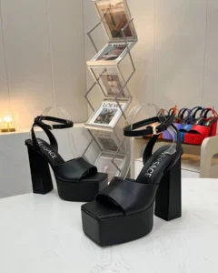 Versace high heels with a sleek black design, featuring a thick platform and block heel, displayed on a table in a stylish setting.