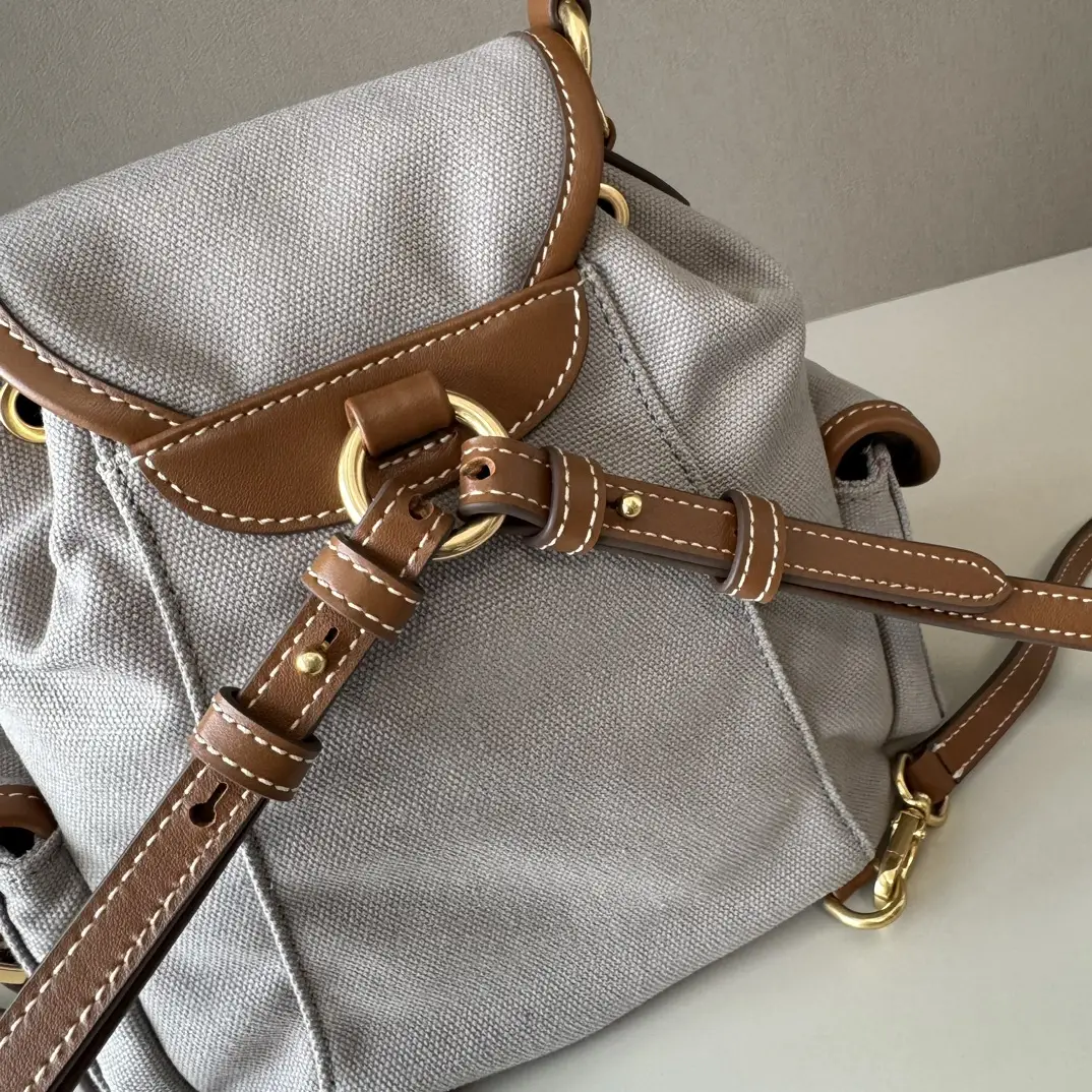 MIU New College Style Backpack featuring a grey canvas body with brown leather accents and adjustable straps, showcasing a stylish and functional design.