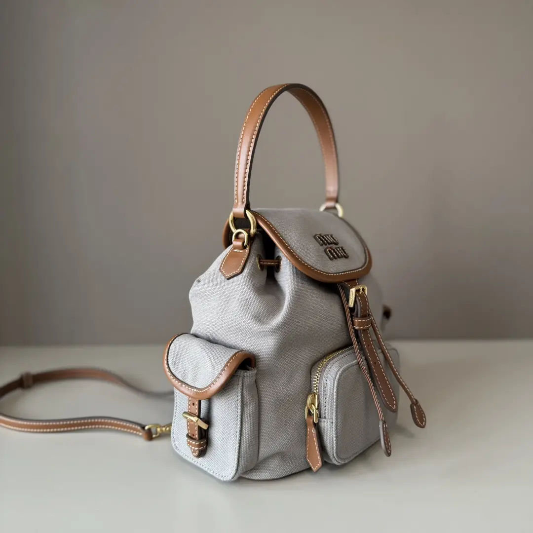 MIU New College Style Backpack in grey canvas with leather accents, featuring multi-pocket design and stylish craftsmanship, ideal for casual wear.