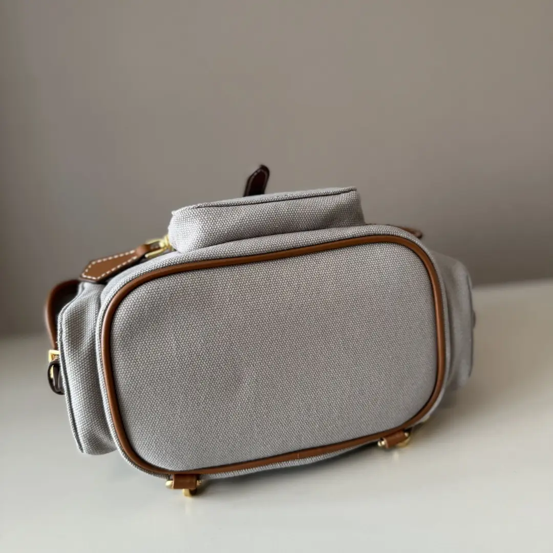 MIU New College Style Backpack in grey canvas with leather accents, showcasing a multi-pocket design and stylish craftsmanship.