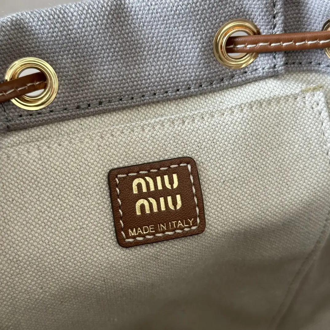 MIU MIU logo tag on a canvas and leather backpack, featuring gold lettering and a "Made in Italy" inscription, highlighting the bag's quality and brand identity.