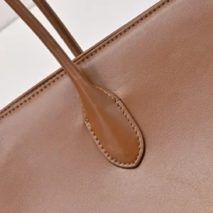 Close-up of The Row Saddle leather shoulder bag showcasing soft brown cowhide leather texture and strap detail.