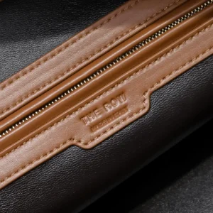 The Row Saddle leather shoulder bag featuring a zipper and logo detail, showcasing soft black leather with contrasting brown accents.