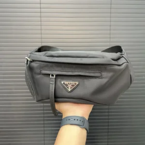 Prada nylon cloth waist bag held in hand, featuring logo and zipper, showcasing sleek design for men and women.
