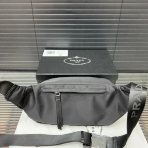 Prada nylon cloth waist bag displayed on a white surface with a black box, featuring a front zipper pocket and adjustable strap showcasing the Prada logo.