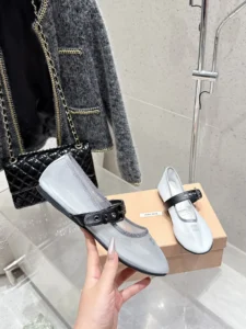 Miu Miu Hollow Weaving Ballet Shoes displayed in hand, featuring soft mesh fabric and black strap, alongside a stylish gray jacket and black handbag, emphasizing luxury and feminine aesthetic.