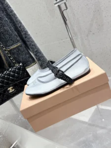 Miu Miu Hollow Weaving Ballet Shoes displayed on a beige box, featuring a soft mesh fabric and a black strap, alongside a stylish black quilted handbag.