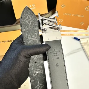Men's L0UIS VUITT0N Donkey belt featuring a black canvas design with LV monogram and silver hardware, held by a gloved hand, with branded packaging in the background.