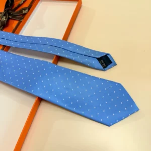 Hermès Letter Men's Tie in light blue with white polka dots, displayed on a contrasting orange background, emphasizing its stylish design and premium quality.