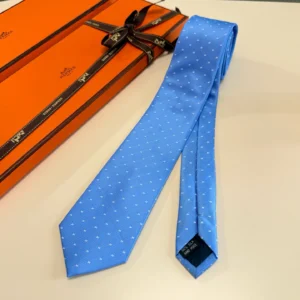 Hermès Letter Men's Tie in blue with white polka dots, displayed alongside an orange Hermès gift box, emphasizing luxury and style.