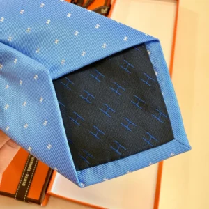 Hermès Letter Men's Tie showcasing a blue design with subtle patterns and an elegant black lining featuring repeated 'H' logos, presented in a stylish setting.