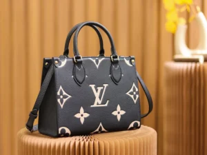 Onthego PM Bicolor Monogram Empreinte Leather Bag by Louis Vuitton, featuring a black and beige design, displayed elegantly on a textured surface.