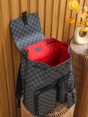 Discovery Backpack in Monogram Eclipse canvas with open top, featuring red interior and multiple compartments, displayed on a textured surface.