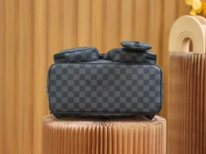 Discovery Backpack in Monogram Eclipse canvas, featuring a checkered pattern, dual top handles, and a structured design, displayed on a textured pedestal.