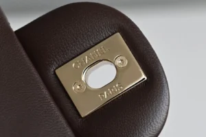Chanel bag close-up gold metal clasp engraved logo dark brown pebbled leather detail