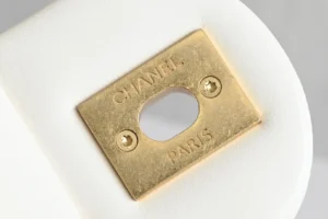 Chanel accessory gold-tone metal plate engraved with Chanel Paris on white textured background