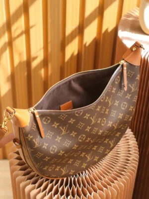 Montaigne BB Monogram canvas handbag with brown and gold design, featuring leather straps and a spacious interior, displayed on a textured background.