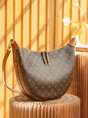 Montaigne BB Monogram canvas handbag featuring a crescent shape, Louis Vuitton logo pattern, and leather accents, displayed on a textured pedestal with warm lighting.