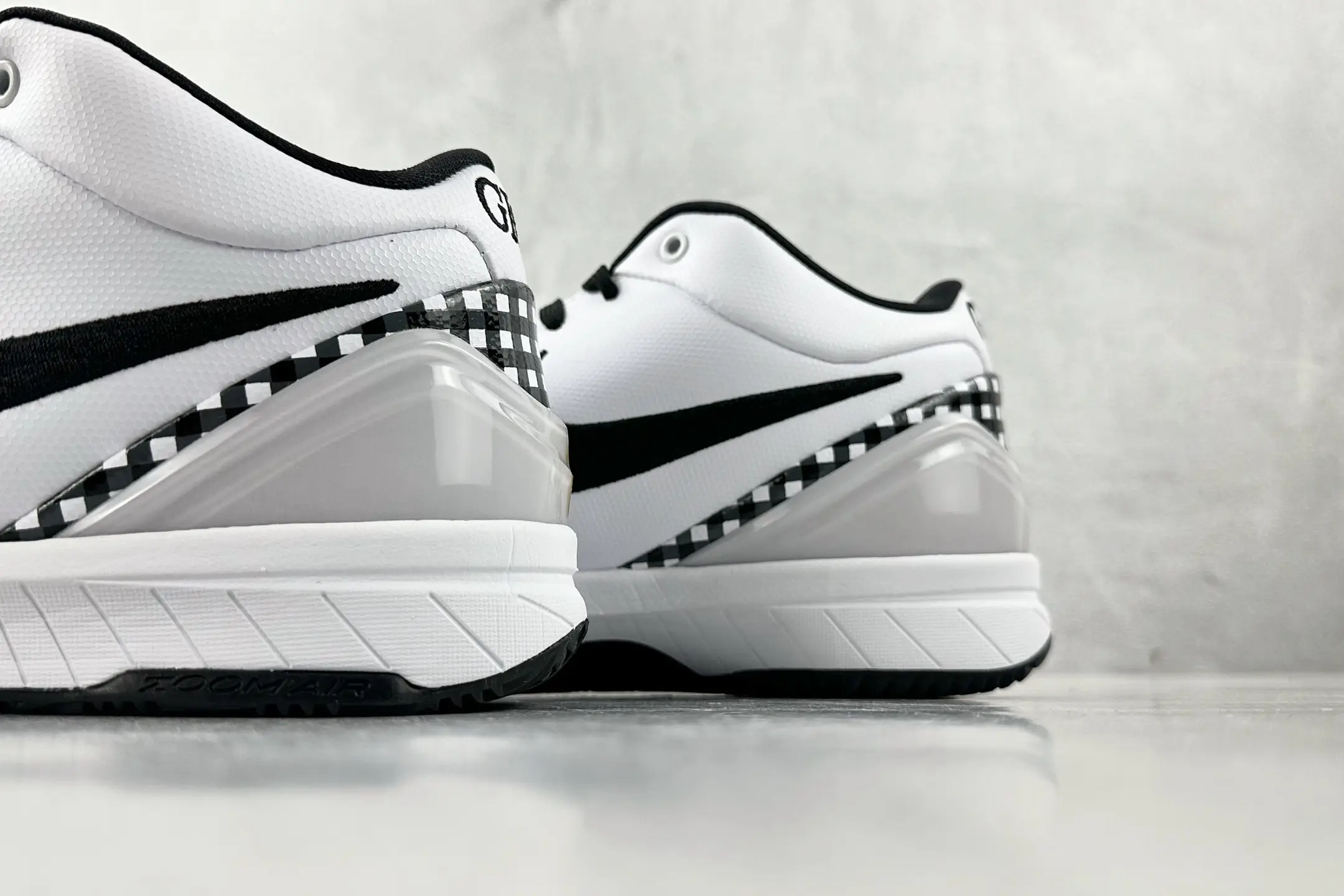 Nike Zoom Kobe 4 "Mambacita" G sneakers featuring a white and black color scheme, checkered detailing on the heel, and a transparent midsole, displayed on a light gray surface.