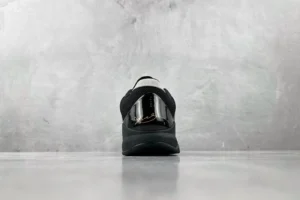 Nike Zoom Kobe 5 Black Knight sneaker viewed from the back against a textured gray background, showcasing its sleek design and reflective elements.