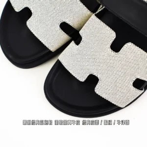 Hermes Aima slippers in black and white, featuring a classic H-shaped design, showcasing premium materials and craftsmanship, available for purchase on an e-commerce platform specializing in high-end replicas.