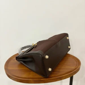 Hermes Kelly Lakis 28 bag in ebony and gold, displayed on a wooden table, showcasing its elegant design and craftsmanship.