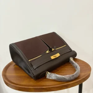 Hermes Kelly Lakis 28 bag in ebony and gold displayed on a wooden table, featuring a structured design and gold hardware.