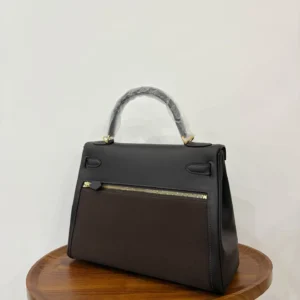 Hermes Kelly Lakis 28 bag in ebony and gold, displayed on a wooden surface, showcasing its elegant design and craftsmanship.
