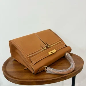 Hermes Kelly Lakis 28 handbag in gold brown leather with gold buckle on a wooden table, showcasing premium craftsmanship and design.